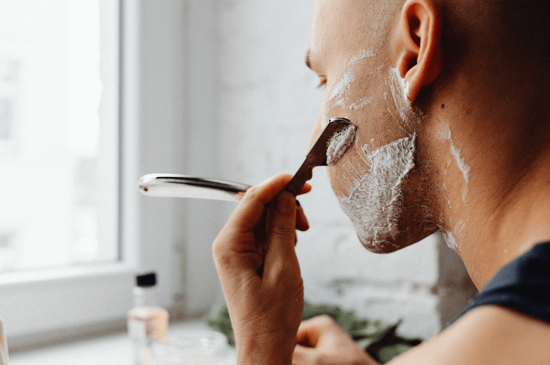 A man, after dry shaving his face, thinking if he should moisturize after shaving to combat dry skin and discomfort. 