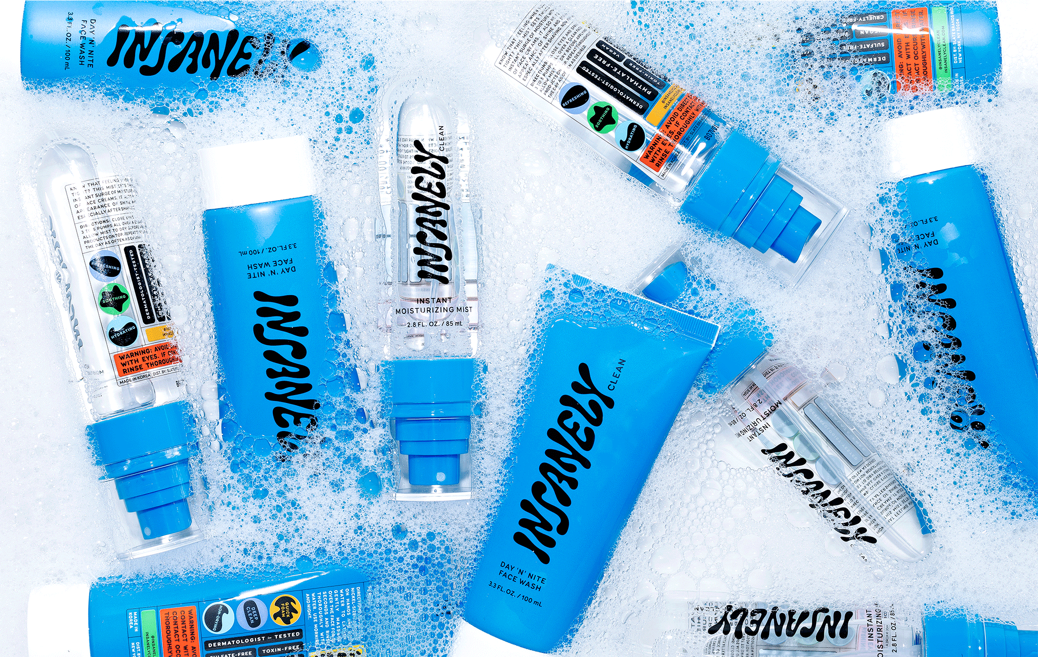 Multiple bottles of Insanely Clean Day 'N' Nite Face Wash and Instant Moisturizing Mist resting in a pool of bubbles.