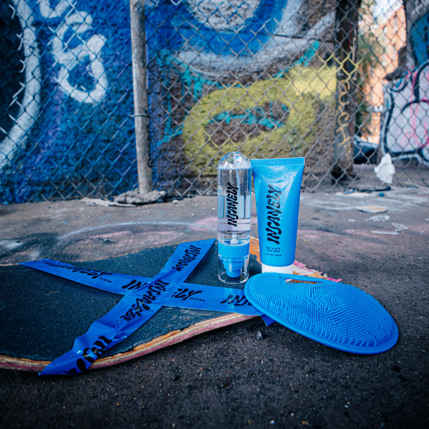 The Insanely Clean Scrubber, Day 'N' Nite Face Wash, and Instant Moisturizing Mist displayed on a skateboard at a skate park.