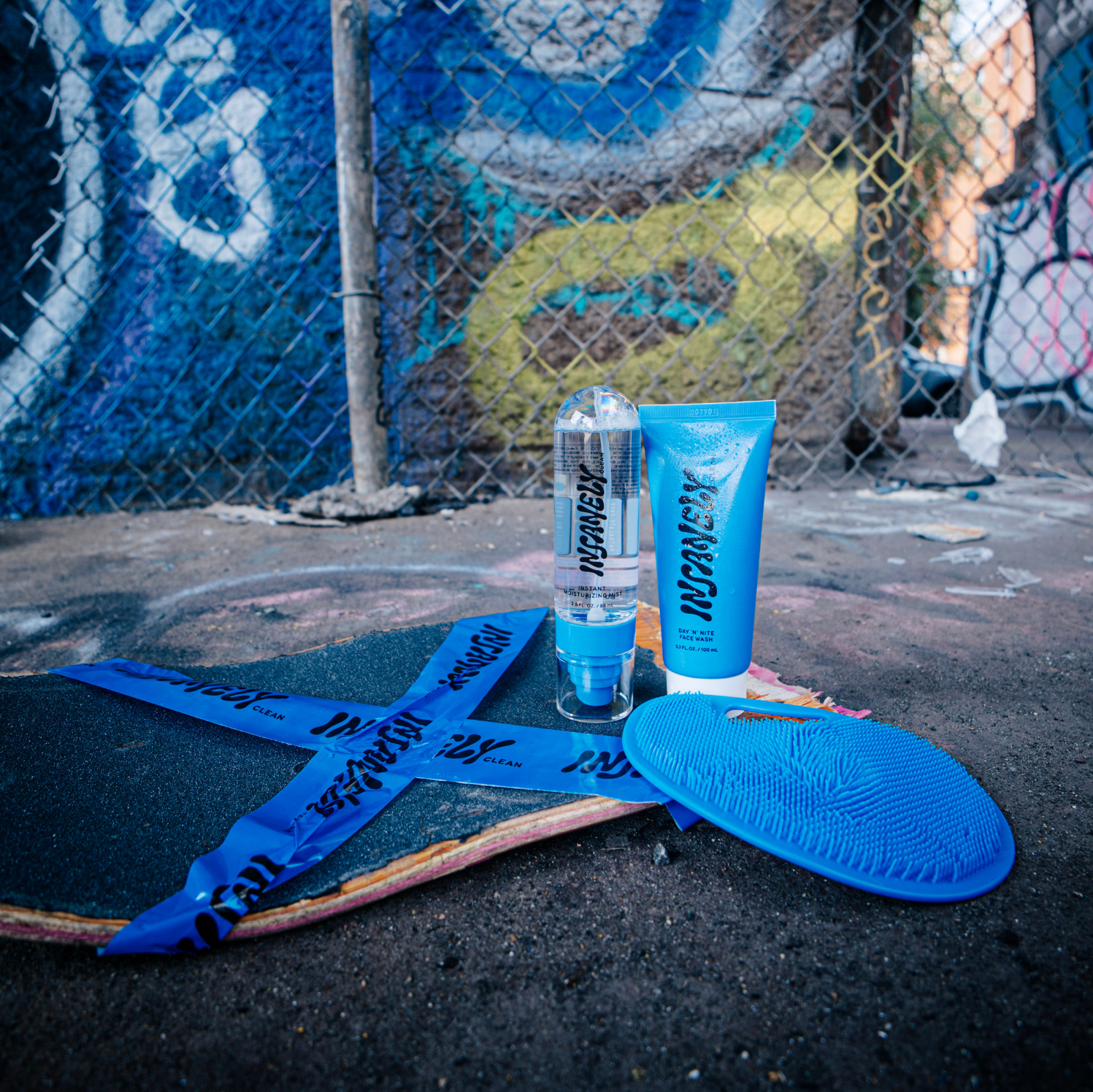 The Insanely Clean Body Scrubber, Day 'n' Nite Face Wash, and Instant Moisturizing Mist displayed on a skateboard at a skate park.