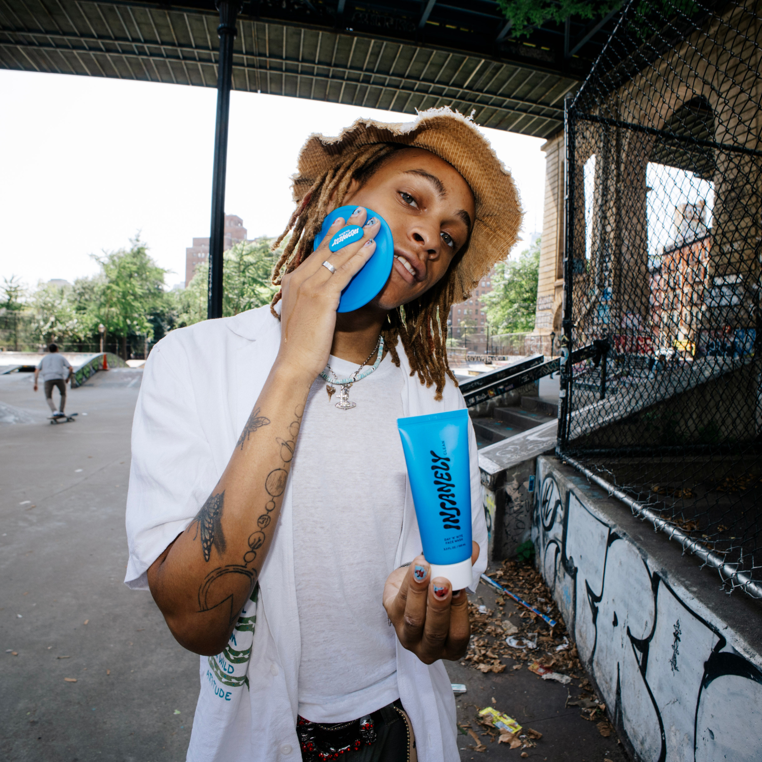 A man at a skate park using the Insanely Clean Body Scrubber on his face while holding the Insanely Clean Day 'n' Nite Face Wash in his other hand.