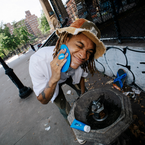 A man scrubbing his face with the Insanely Clean Scrubber with the Day 'N' Nite Face Wash resting by a water fountain at a skate park.